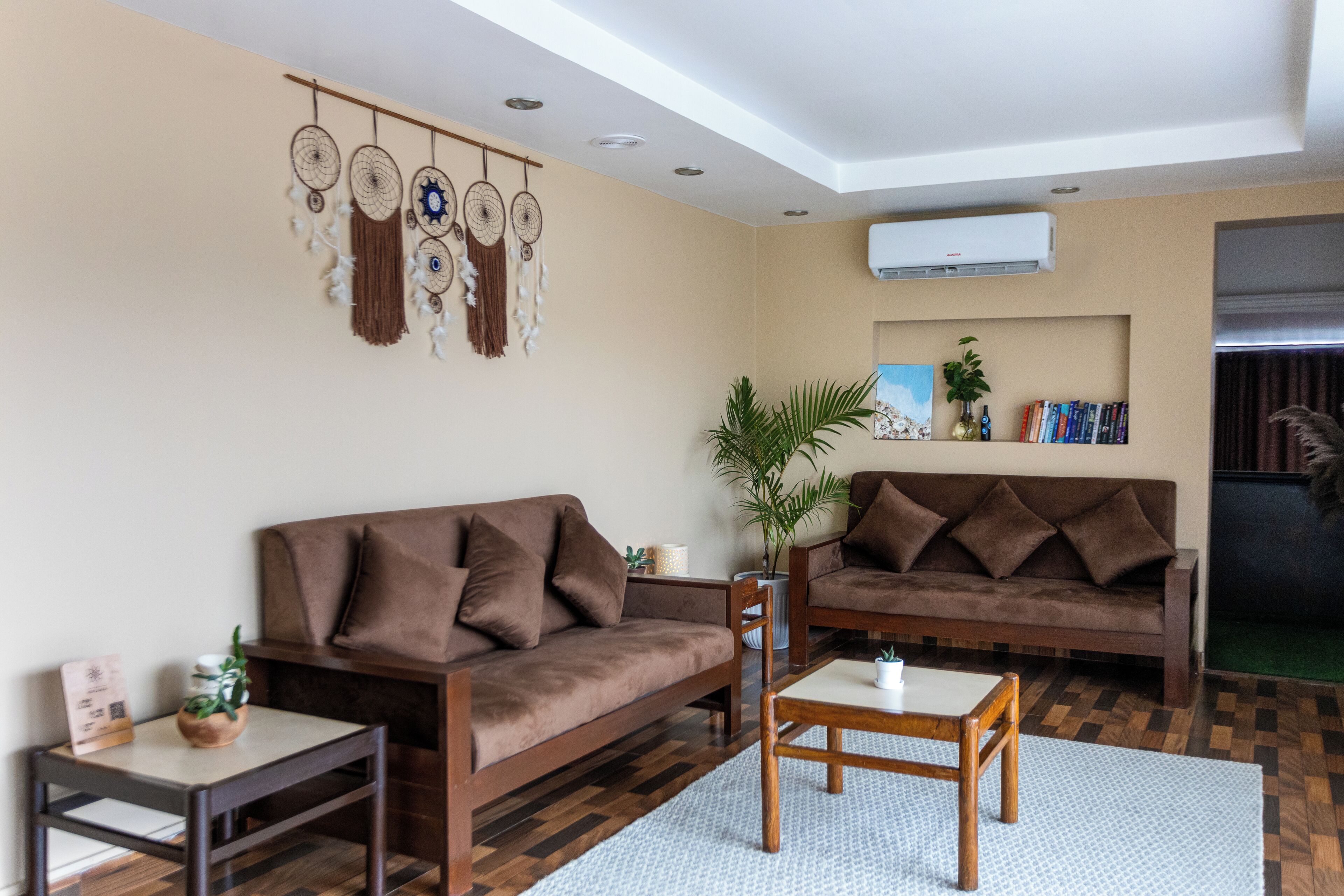 A living room with two brown sofas, a coffee table, a side table, a plant, and a dreamcatcher wall hanging.