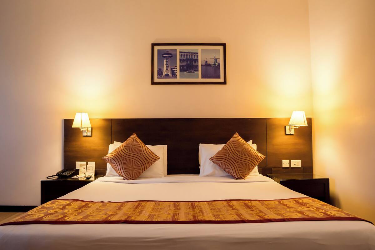 A hotel room with a large bed, two nightstands, a framed picture above the bed, and two wall-mounted lamps.