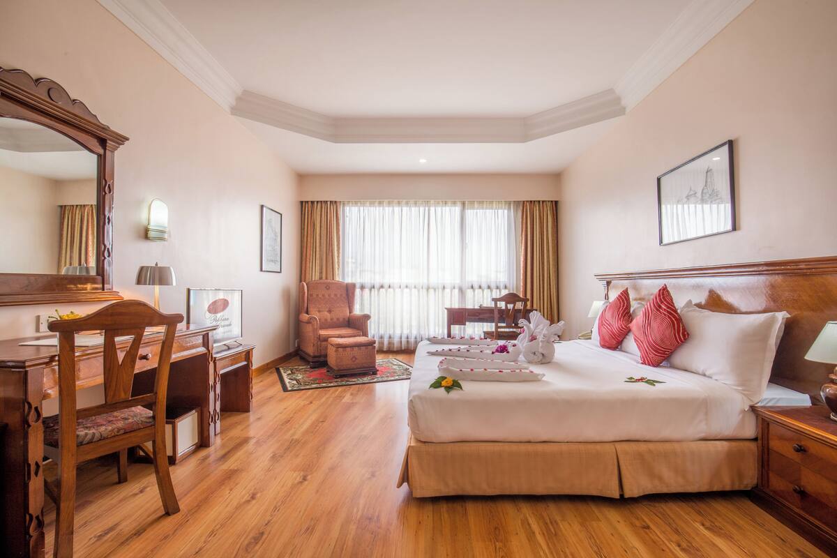 A hotel room with a large bed, a desk, a chair, a mirror, and a window with curtains.