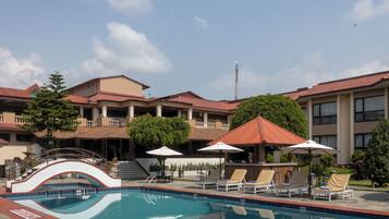 A hotel with a swimming pool, lounge chairs, and umbrellas.