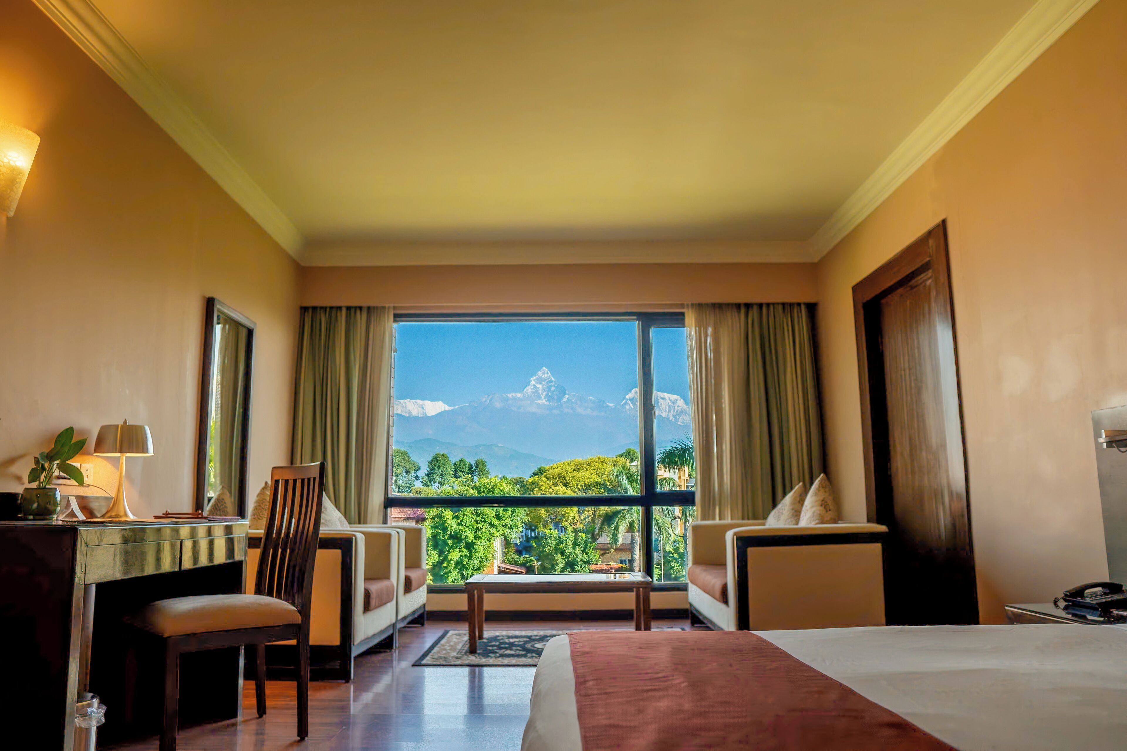 A hotel room with a large window, a bed, a desk, a chair, and a sofa.