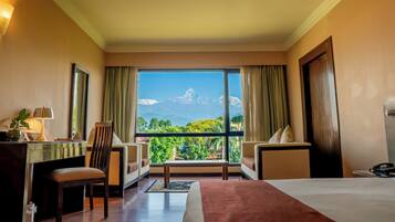 A hotel room with a large window, a bed, a desk, a chair, and a sofa.