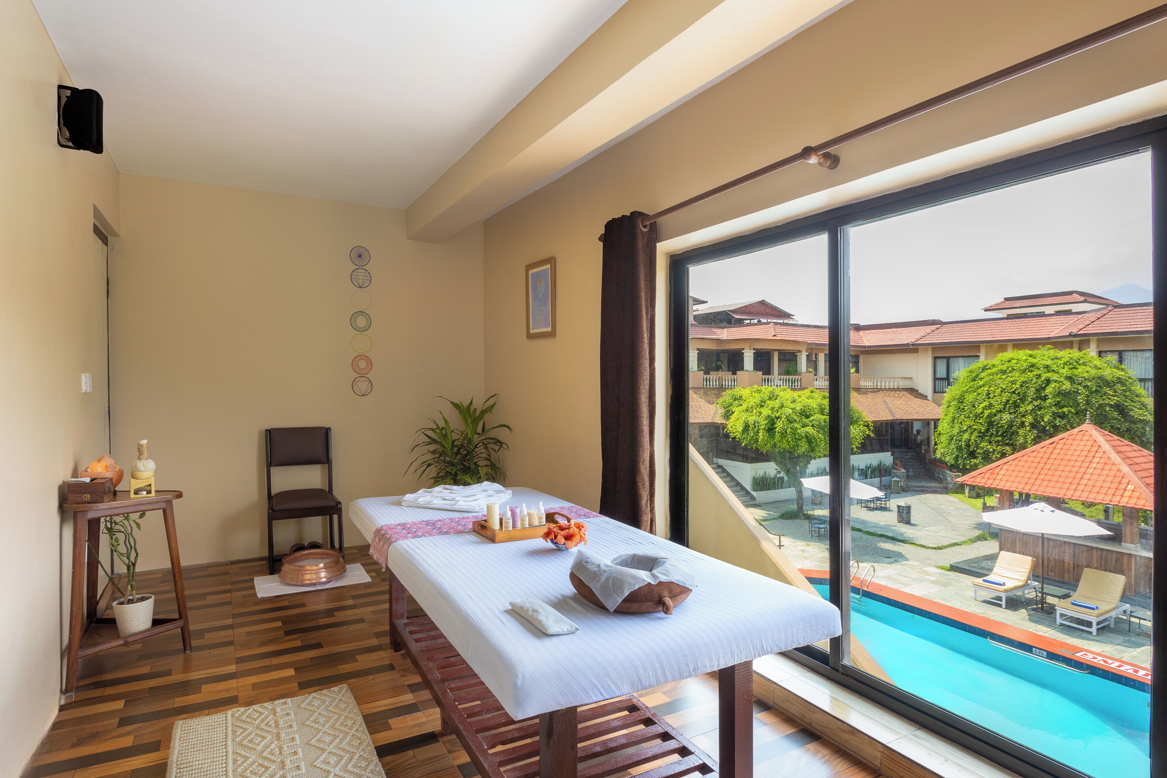 A hotel room with a large window, a wooden floor, a table with toiletries, a chair, and a small plant.