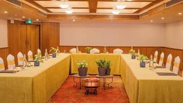 Una sala de conferencias con una mesa larga, sillas, plantas en macetas y una pequeña mesa con un centro de mesa decorativo.