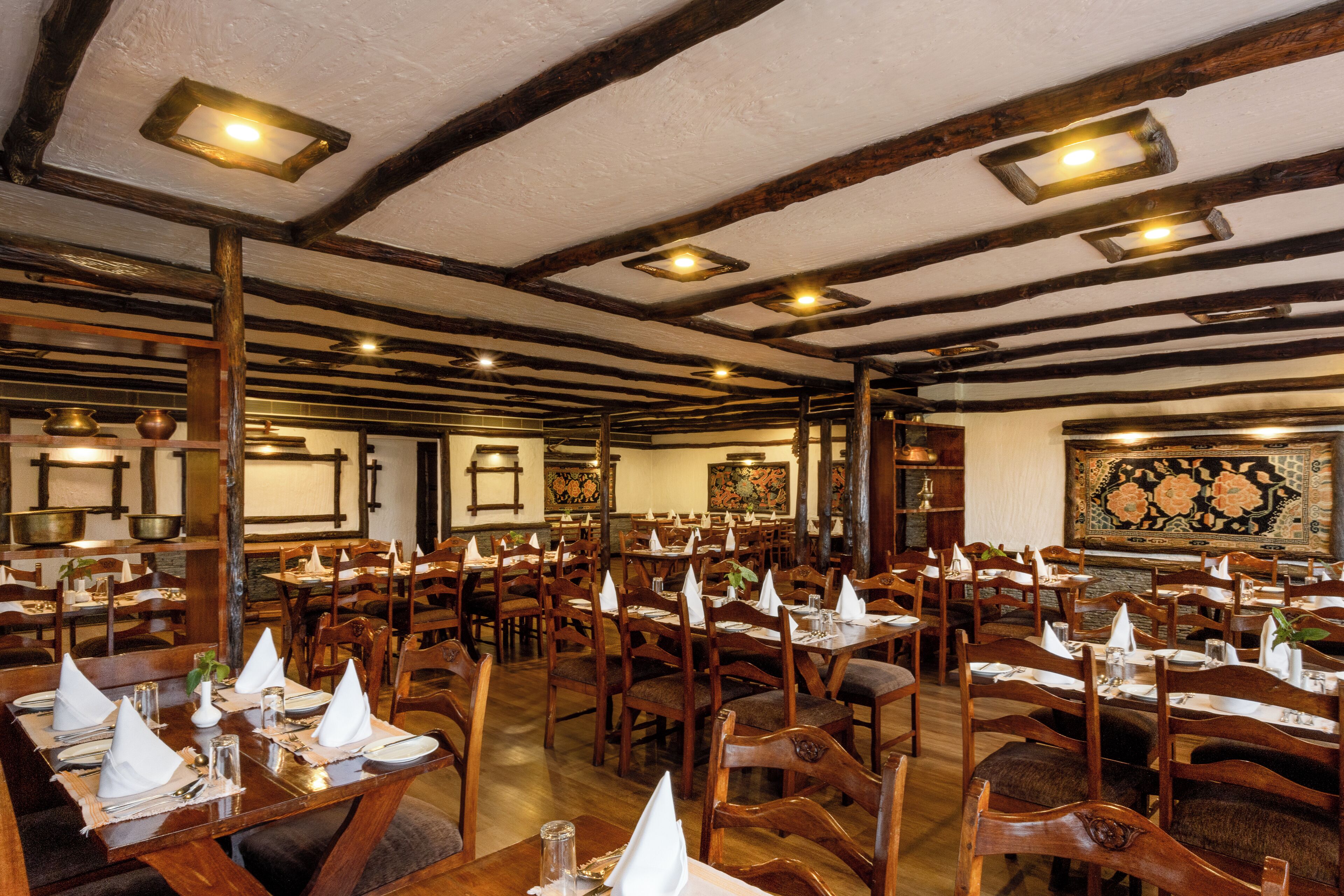 A restaurant with multiple wooden tables and chairs, high ceilings with exposed beams, and traditional decor.