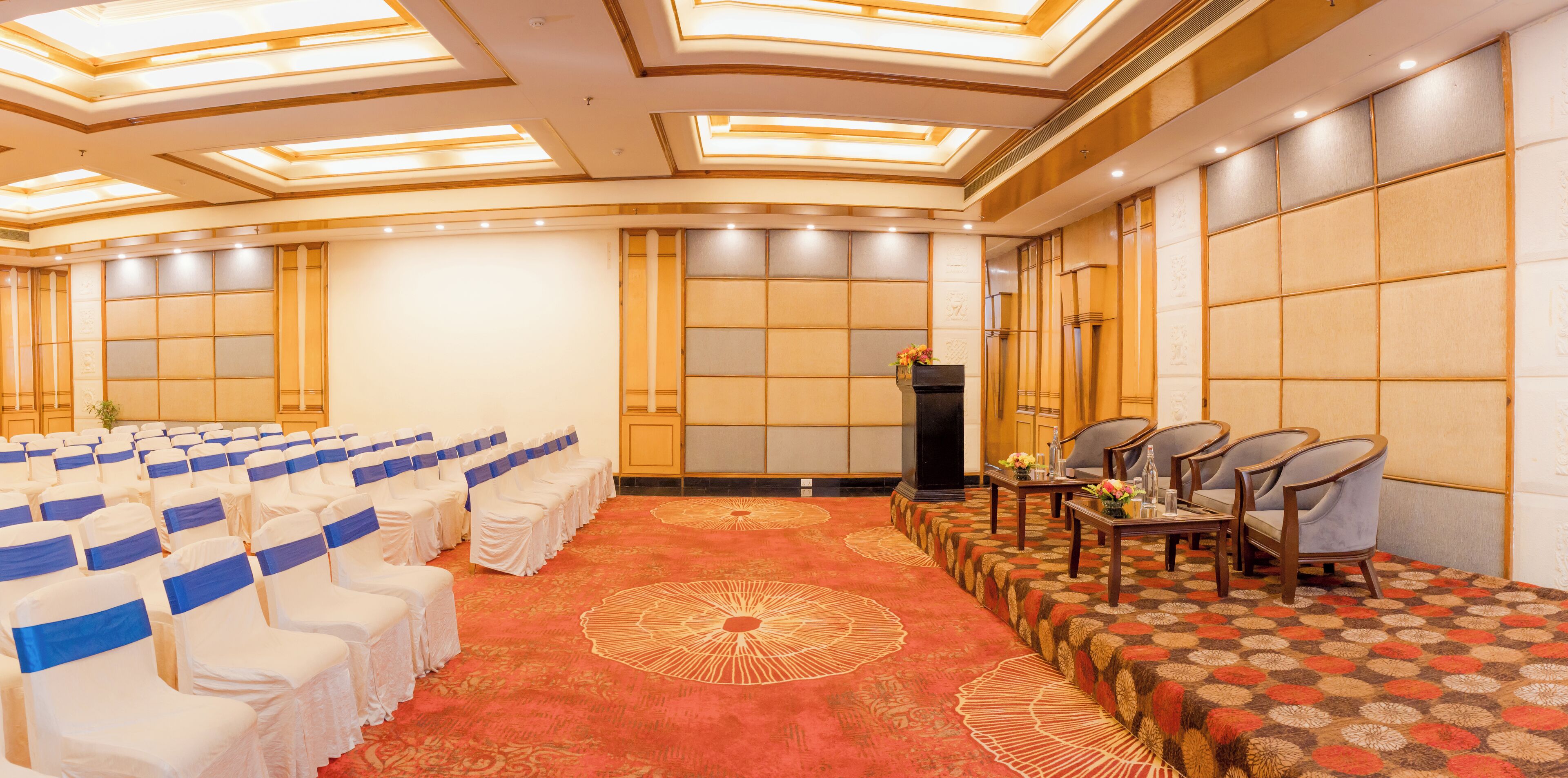 A conference room with rows of chairs, a podium, and a patterned carpet.