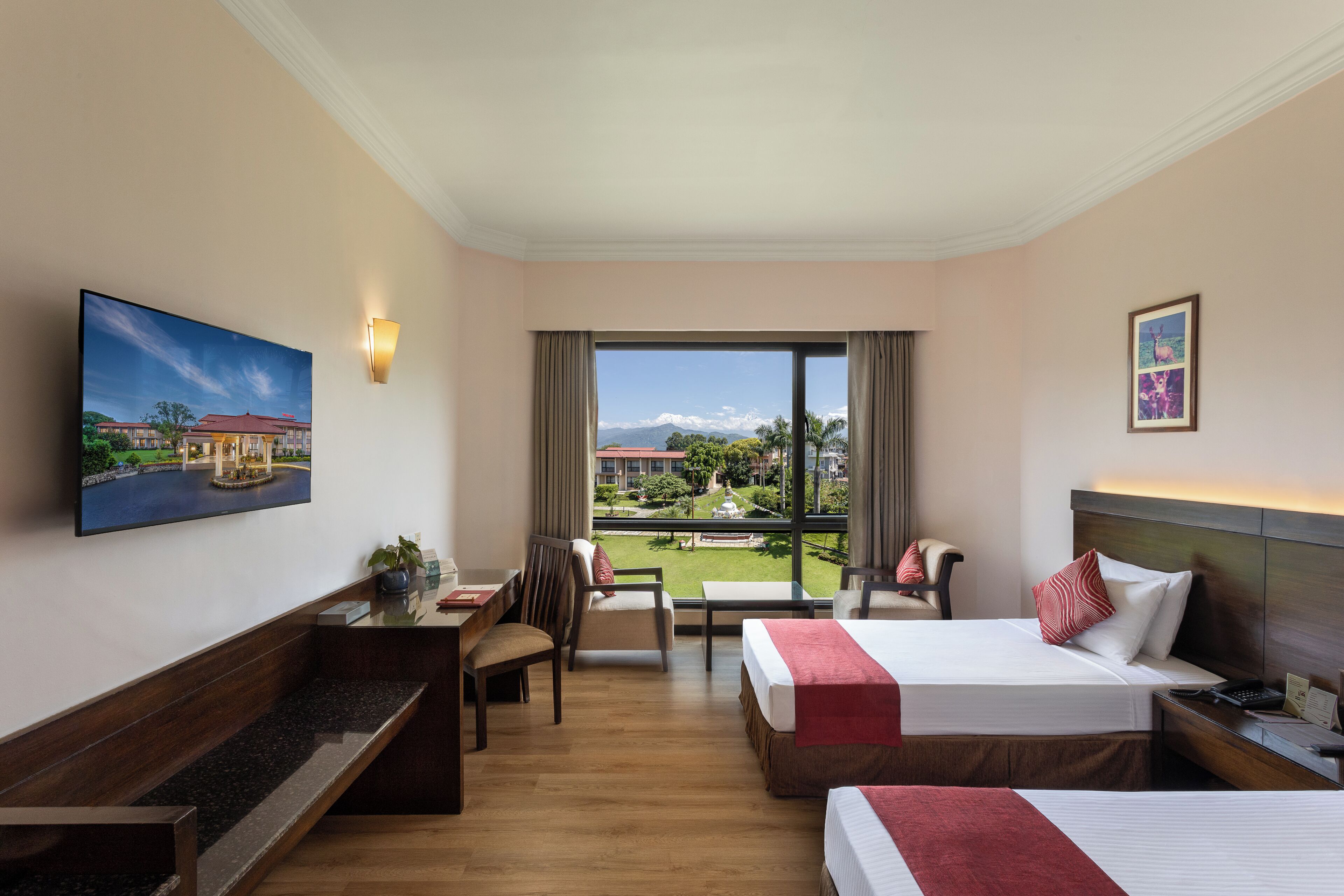 Quarto de hotel com cama, escrivaninha, cadeira e uma janela ampla com vista para um edifício e áreas verdes.