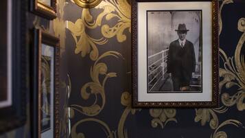 A room with ornate wallpaper, a framed photograph on the wall, and a tufted leather bench.