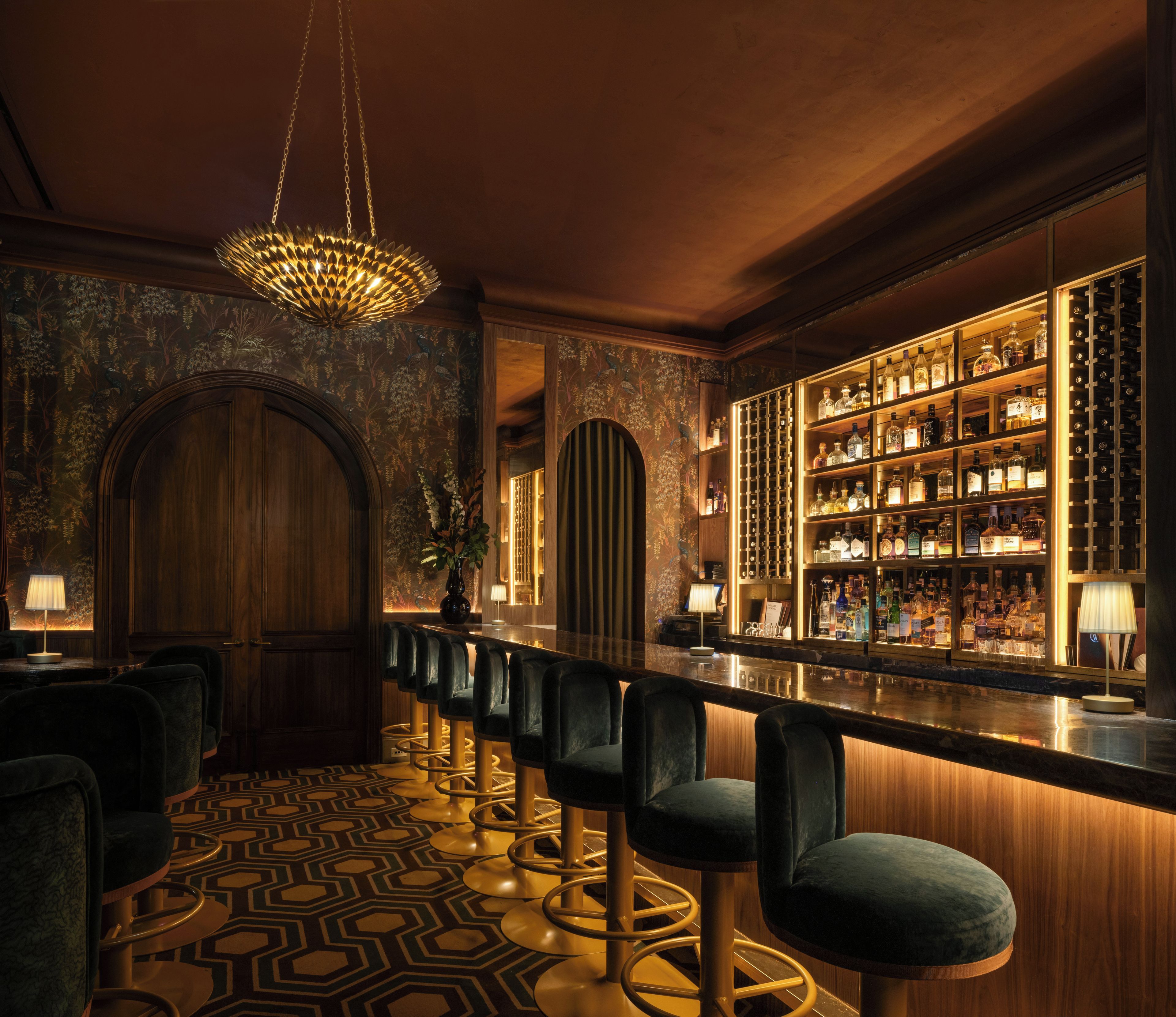 Una zona de bar con una barra larga, varios taburetes y un interior bien iluminado.