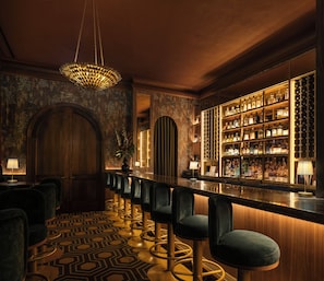 A bar area with a long counter, multiple stools, and a well-lit interior. - Refinery Hotel (New York)