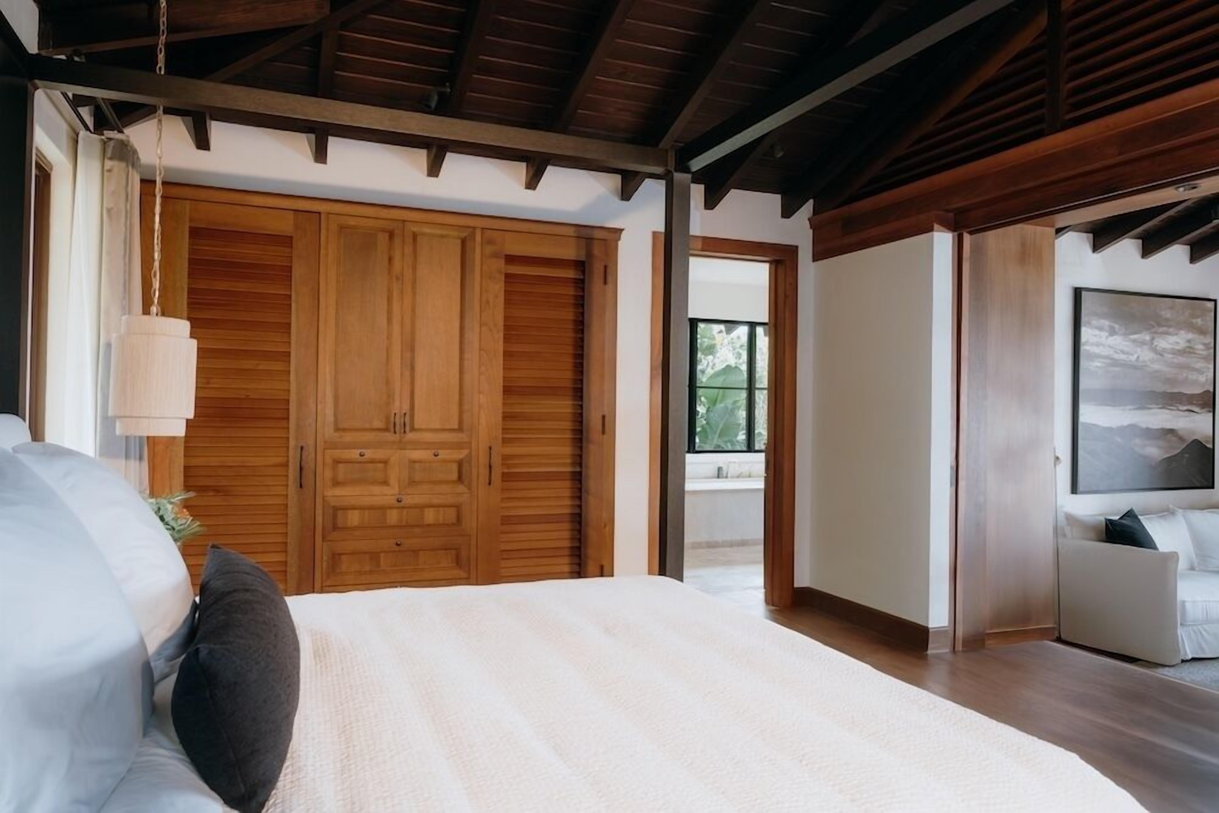 A bedroom with a bed, wooden wardrobe, and a view of the outdoors.