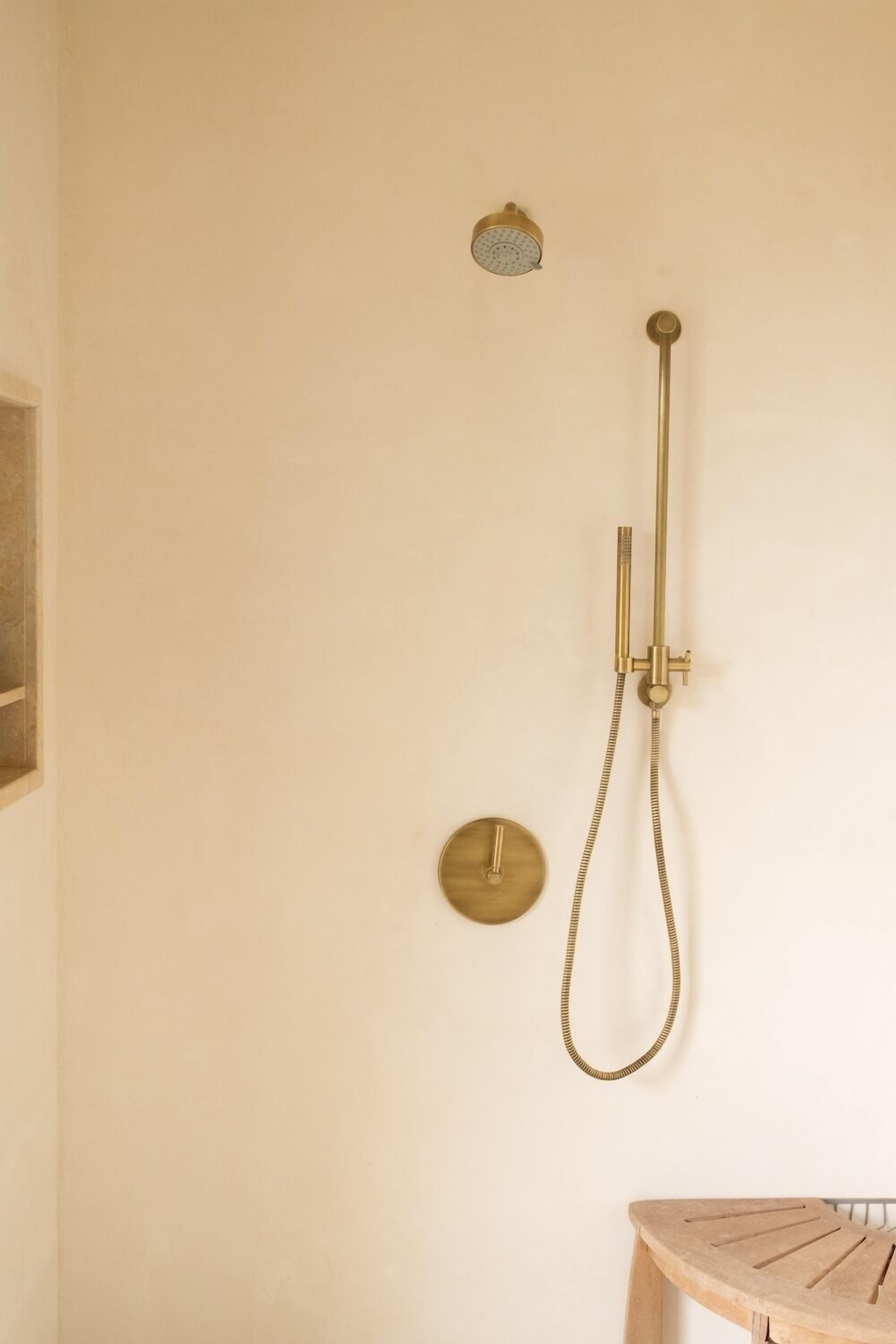 A bathroom with a wall-mounted shower, a round control panel, and a wooden stool.