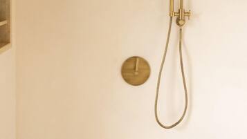 A bathroom with a wall-mounted shower, a round control panel, and a wooden stool.