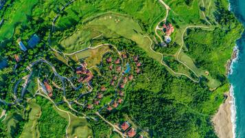 An aerial view of a golf course with multiple bunkers, a winding road, and several buildings with red roofs.