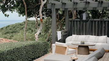 A wooden deck with outdoor furniture, including a sofa and lounge chairs, and a pergola structure.