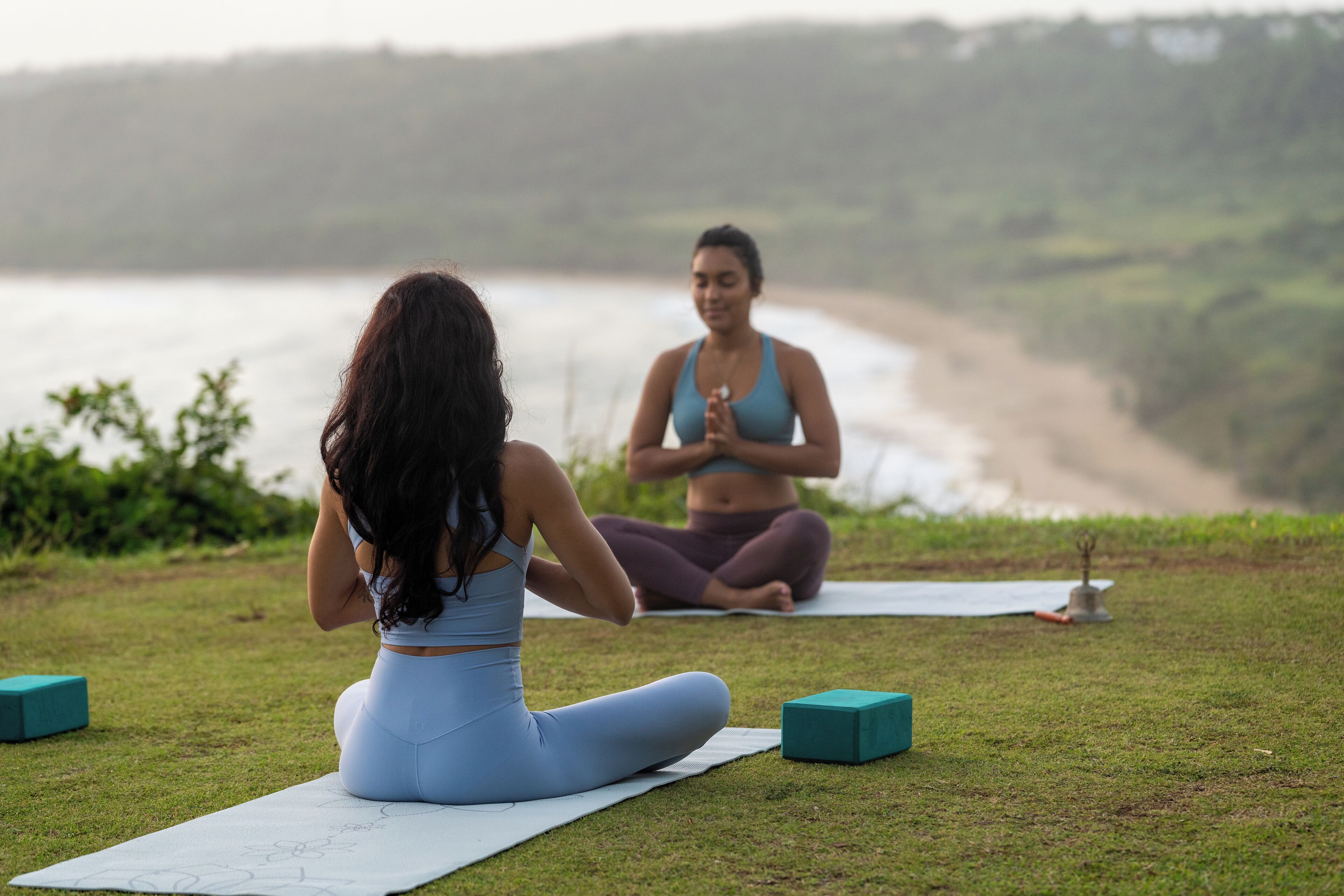 Deux personnes pratiquent le yoga sur une pelouse, avec une plage en arrière-plan.
