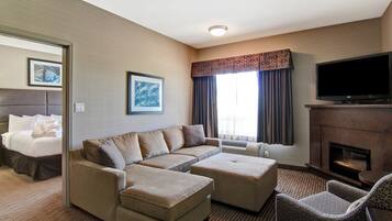 A hotel room with a sectional sofa, a flat-screen TV, a fireplace, and a bed with a headboard.