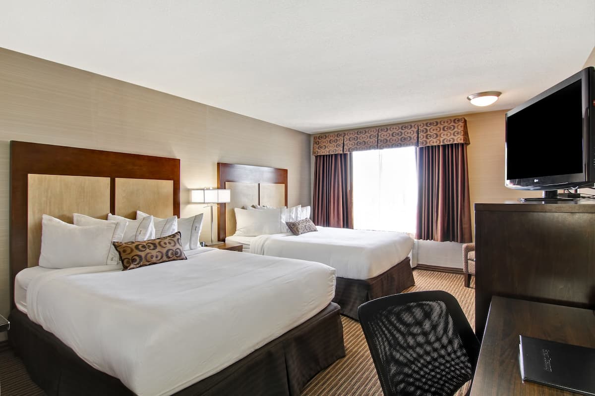 A hotel room with two beds, a TV, a desk, and a chair.