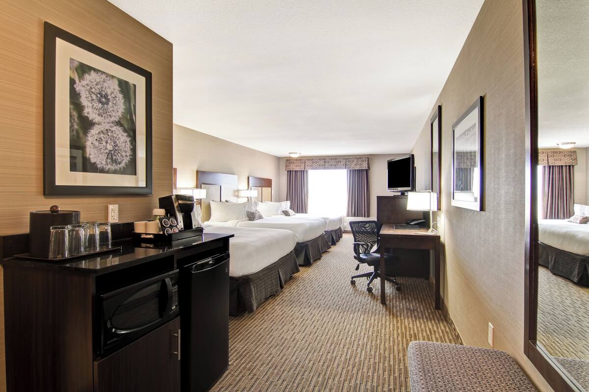 A hotel room with a large bed, a desk with a chair, a television, and a minibar.