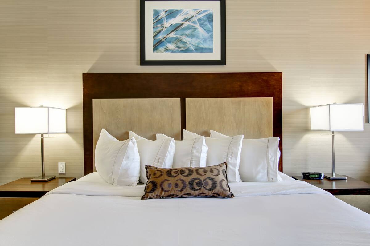 A neatly made bed with white linens and a patterned pillow, flanked by two bedside lamps on wooden nightstands.