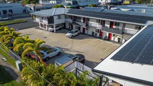 Un edificio de varios pisos con estacionamiento, paneles solares en el techo y un pequeño jardín con palmeras.