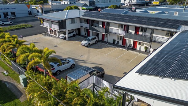 A multi-story building with a parking lot, solar panels on the roof, and a small garden area with palm trees. - Citywalk Motor Inn (Rockhampton)