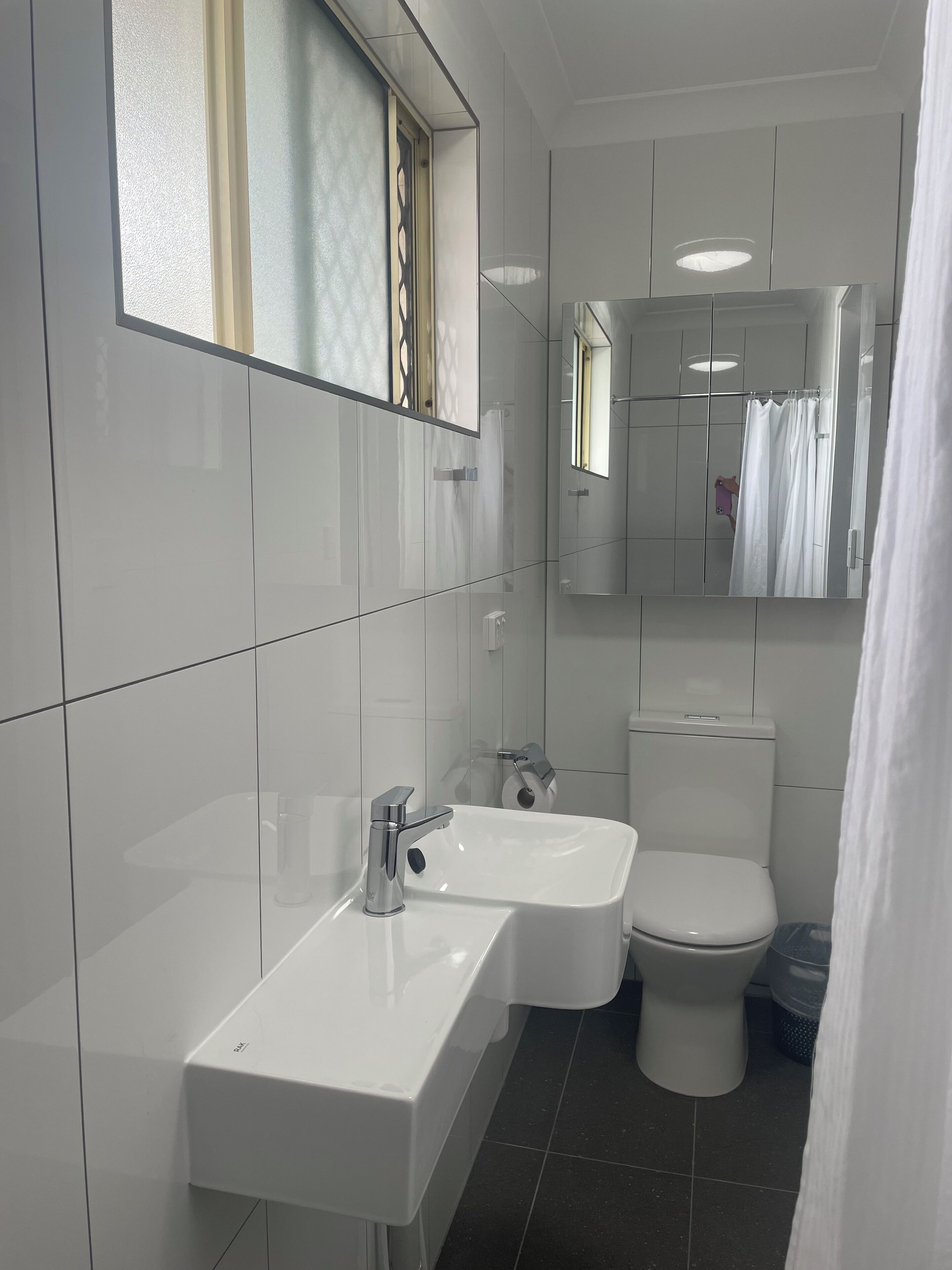 A modern bathroom with a white sink, mirror, and toilet.