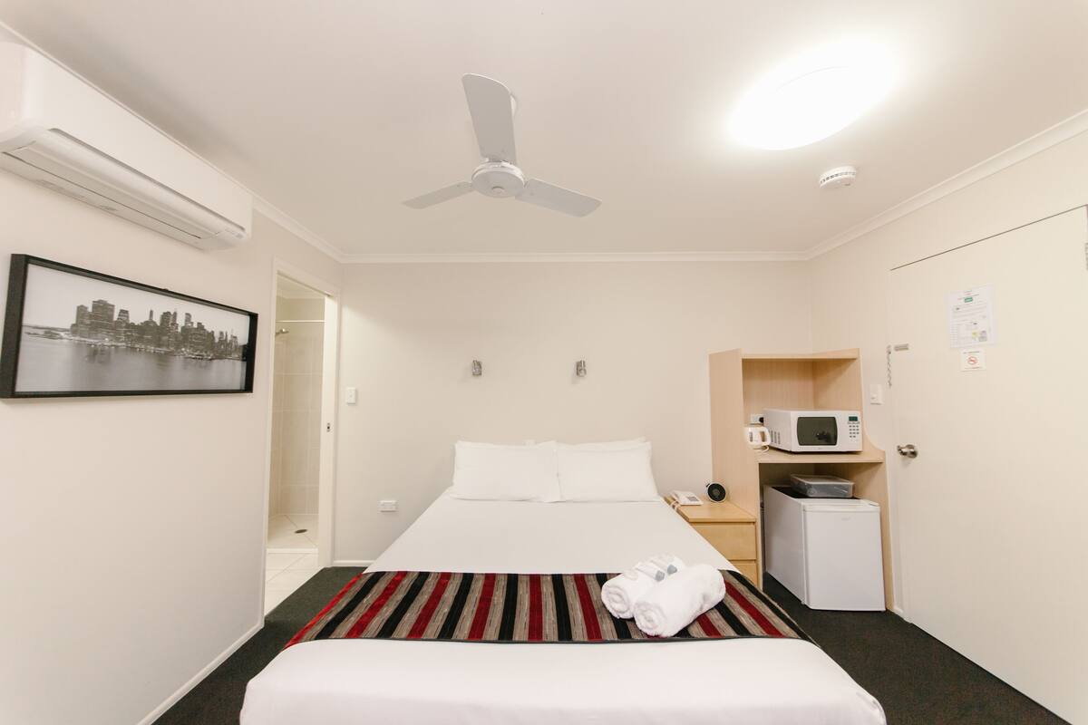 Una habitación de hotel con cama, ventilador de techo, microondas y un refrigerador pequeño.