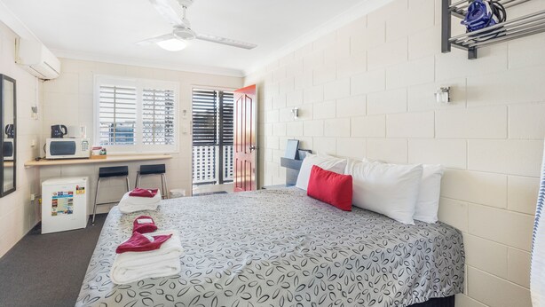 Una habitación de hotel con una cama, un escritorio con computadora, un microondas y un refrigerador pequeño.