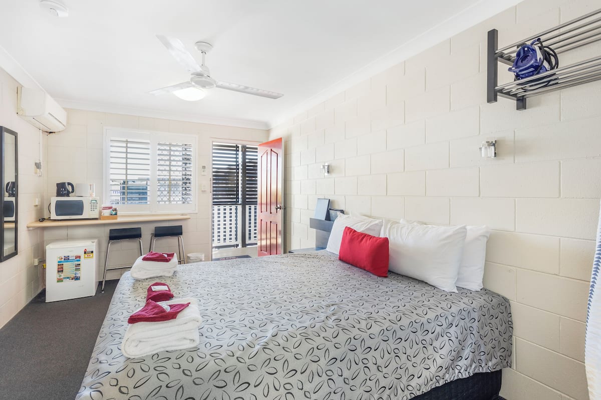 Una habitación de hotel con una cama, un escritorio con computadora, un microondas y un refrigerador pequeño.