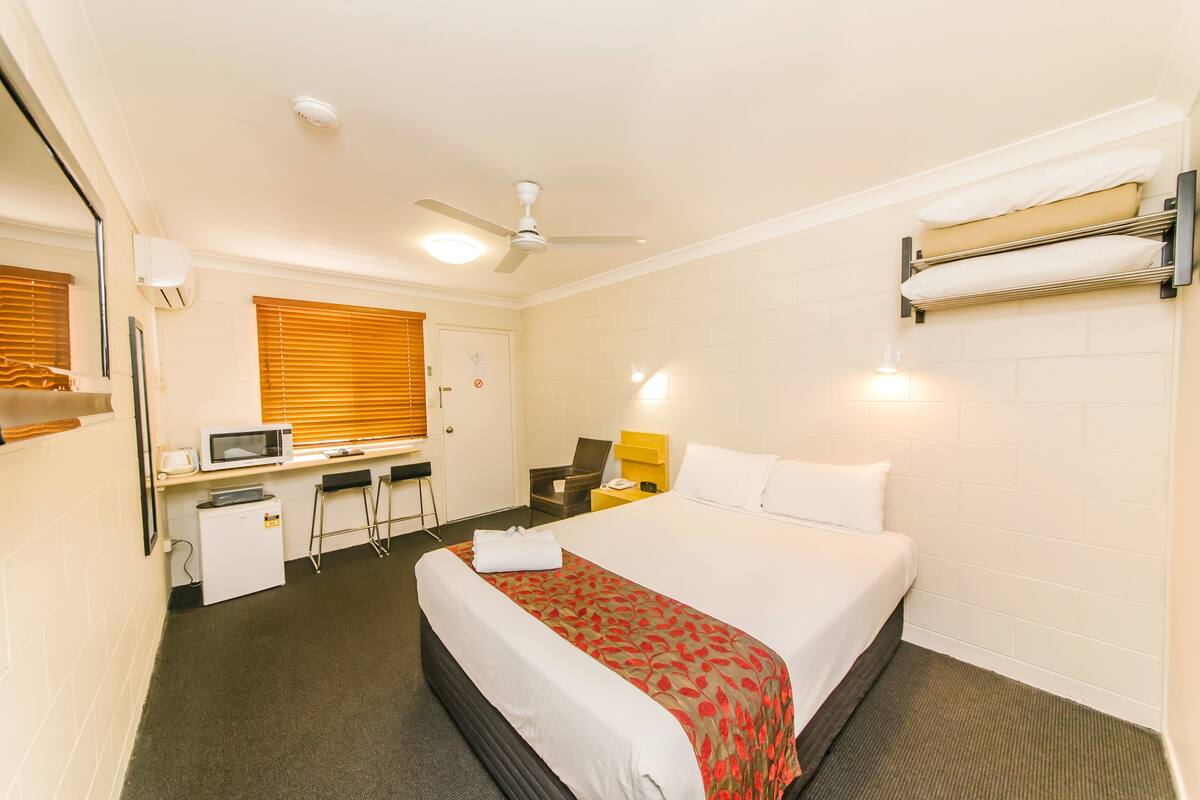 Una habitación de hotel con cama, escritorio, silla, microondas y un refrigerador pequeño.