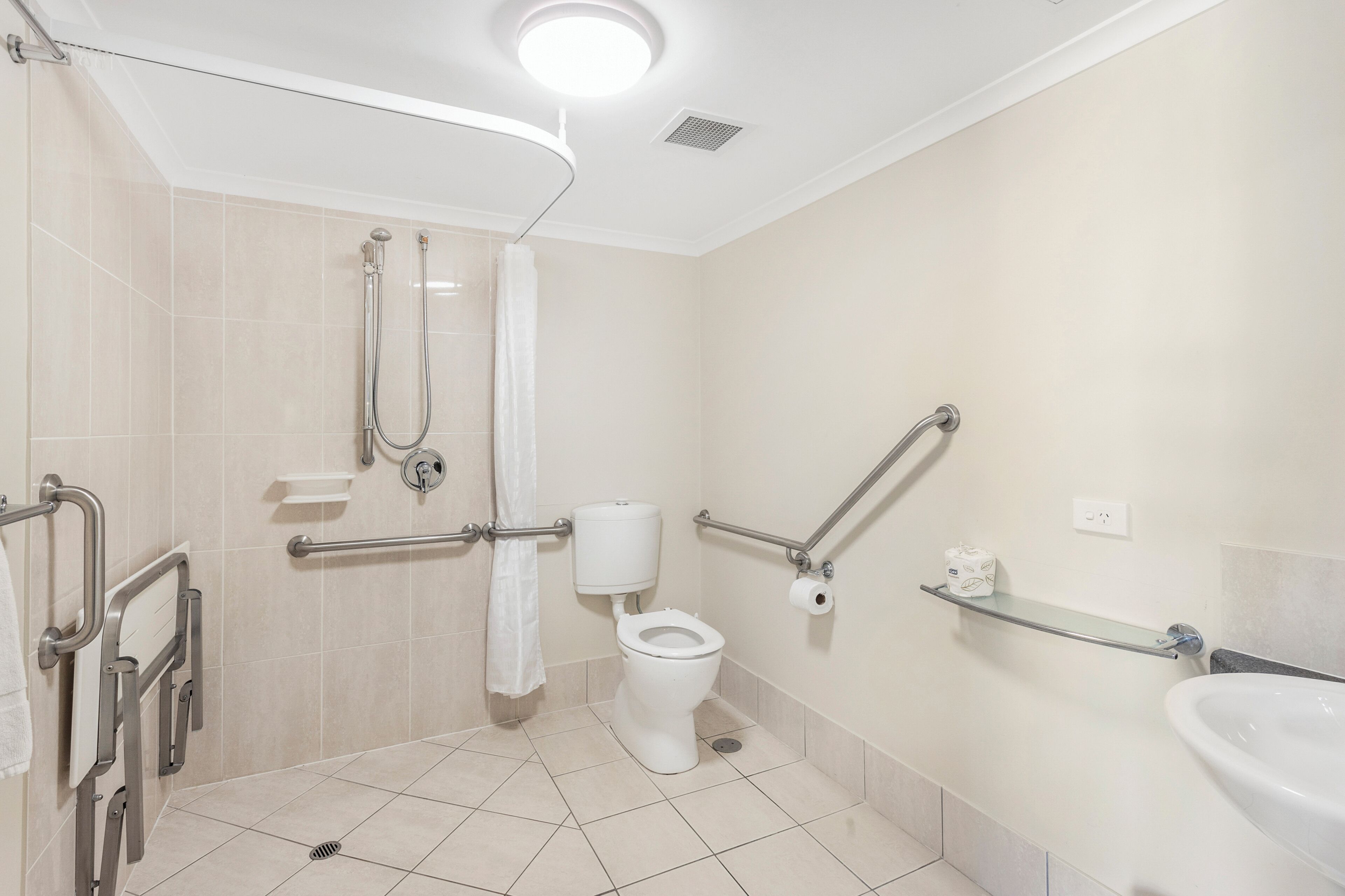 A bathroom with a toilet, shower, grab bars, and a sink.