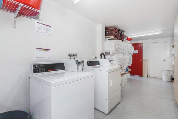 Un cuarto de lavandería con dos lavadoras blancas, una puerta roja y una pila de toallas dobladas.