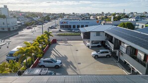 Un estacionamiento con varios coches, un edificio con la etiqueta "MOVE" y paneles solares, y vistas a una zona residencial con casas y palmeras.