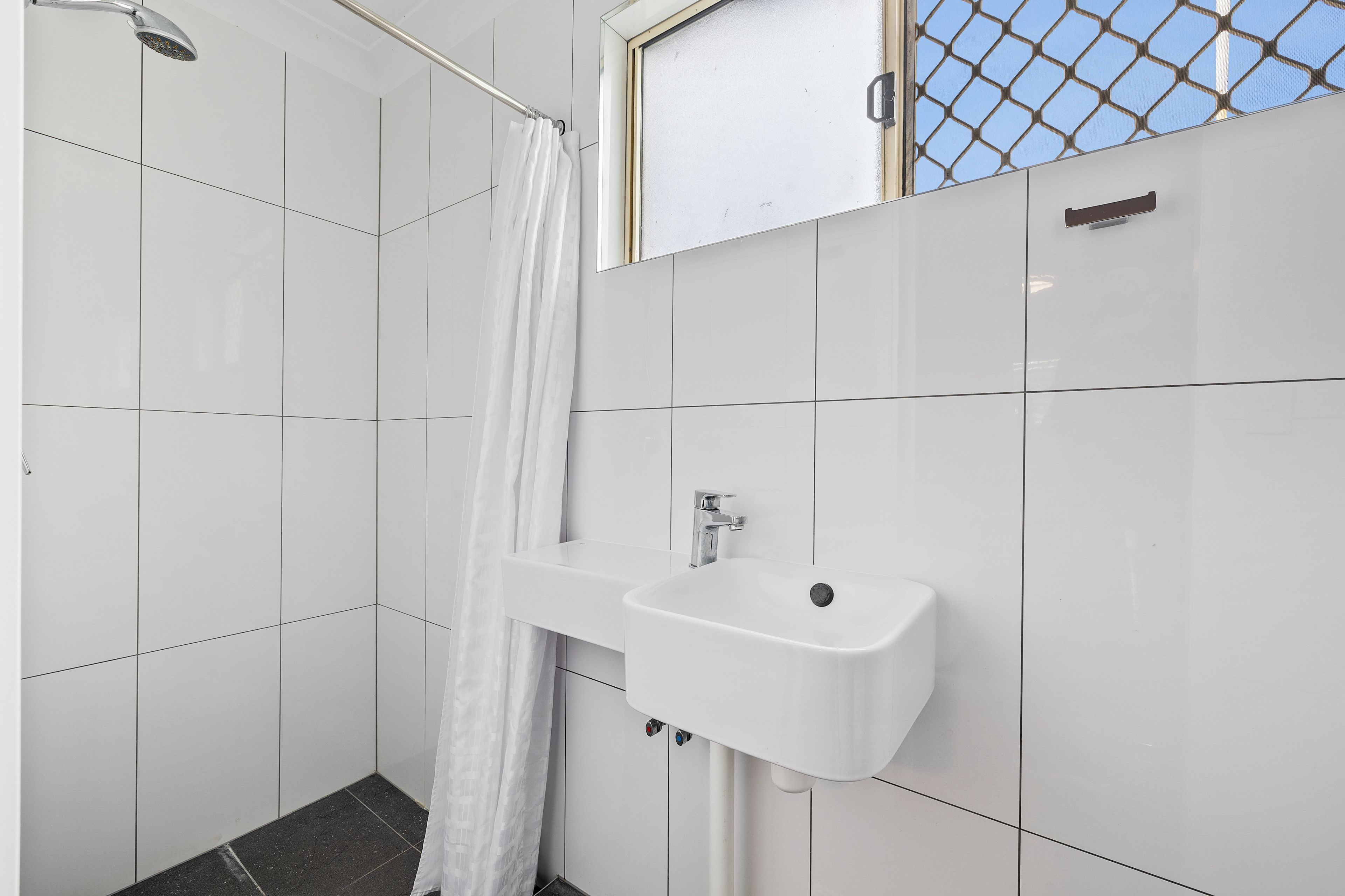 Une salle de bain équipée d’une douche, d’un lavabo et d’une fenêtre avec un moustiquaire.