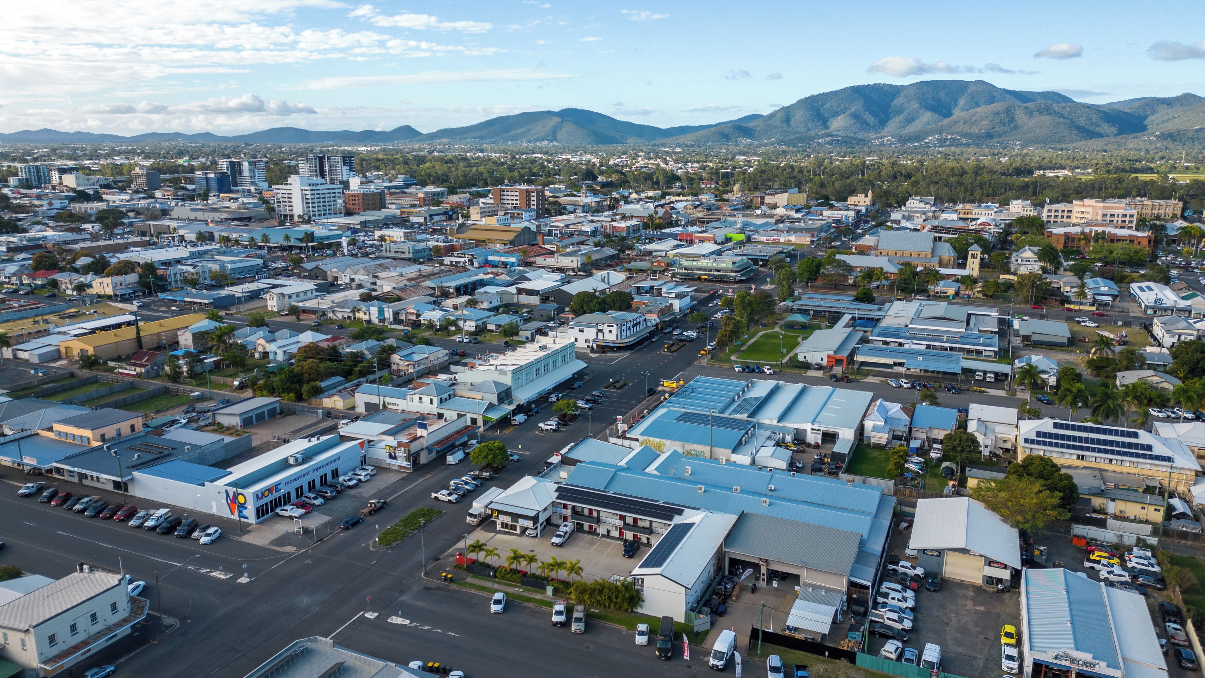 A cityscape with a mix of commercial and residential buildings, a prominent MOVE store, and a mountainous backdrop.