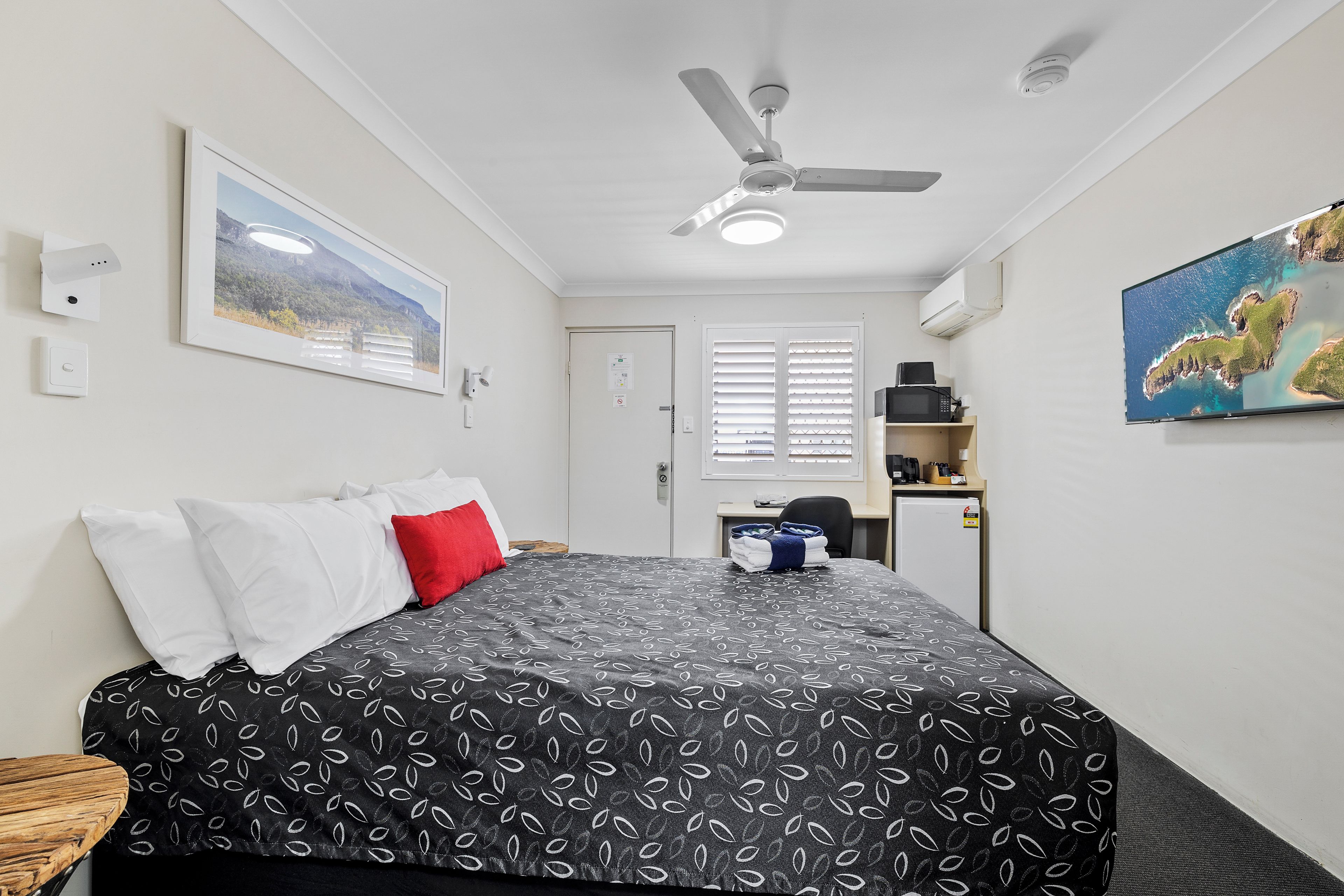 A hotel room with a bed, a ceiling fan, a painting, and a view of the sea.
