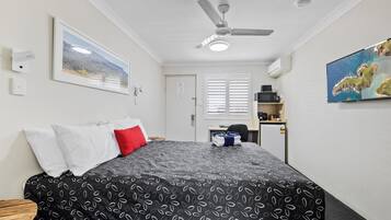 A hotel room with a bed, a ceiling fan, a painting, and a view of the sea.