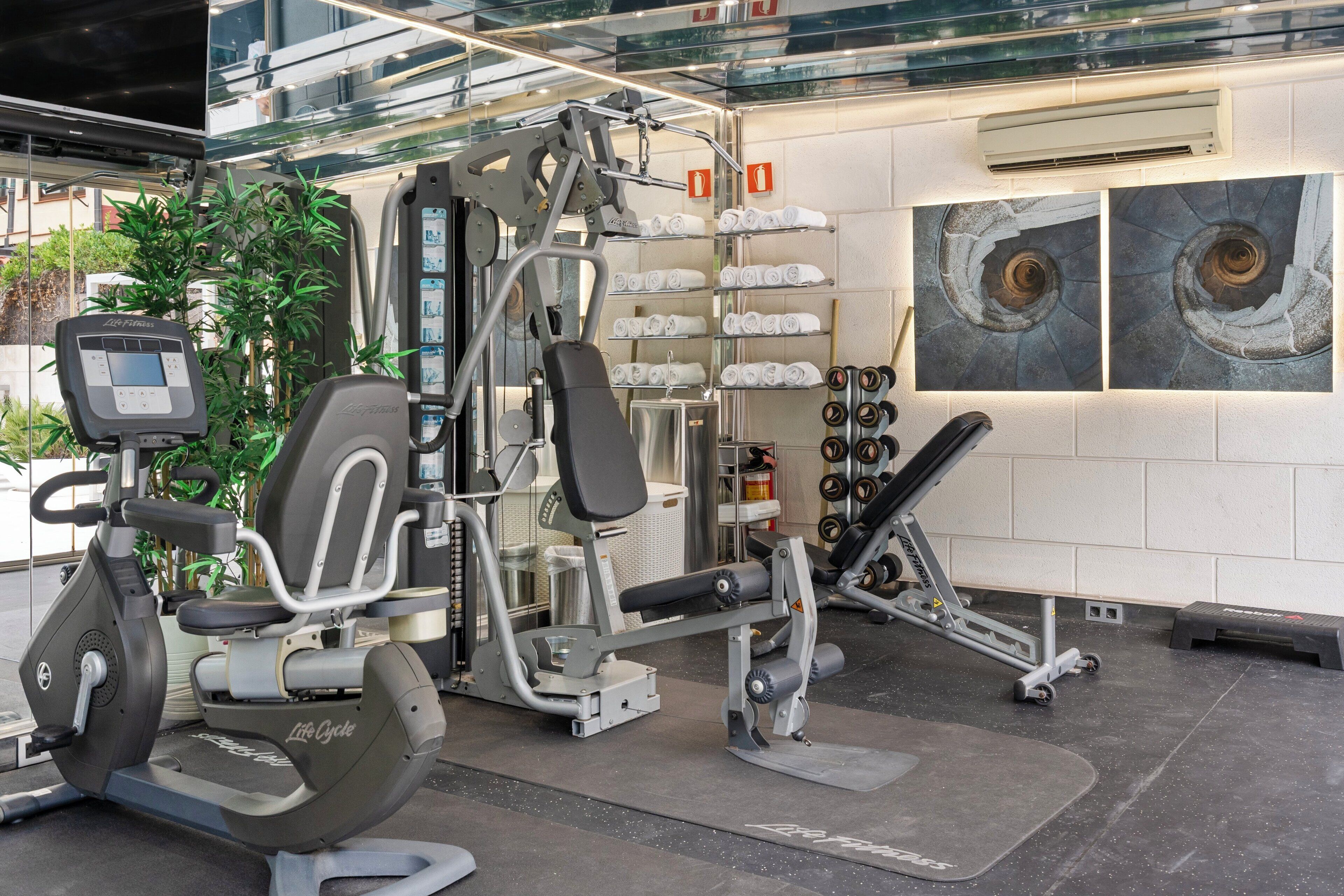 Une salle de sport équipée de machines de cardio, d’appareils de musculation et d’un climatiseur fixé au mur.