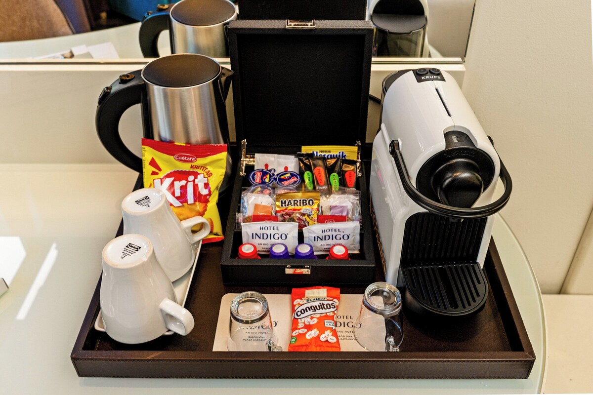 Un plateau avec une cafetière, deux tasses blanches, une boîte contenant des articles de toilette d’hôtel et un autre plateau avec des en-cas.