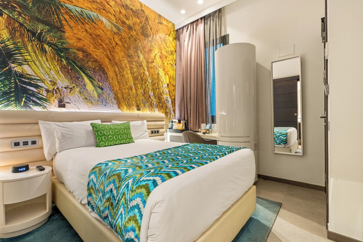 Une chambre d’hôtel avec un grand lit, une table de chevet, un bureau, une armoire et une grande fresque murale.