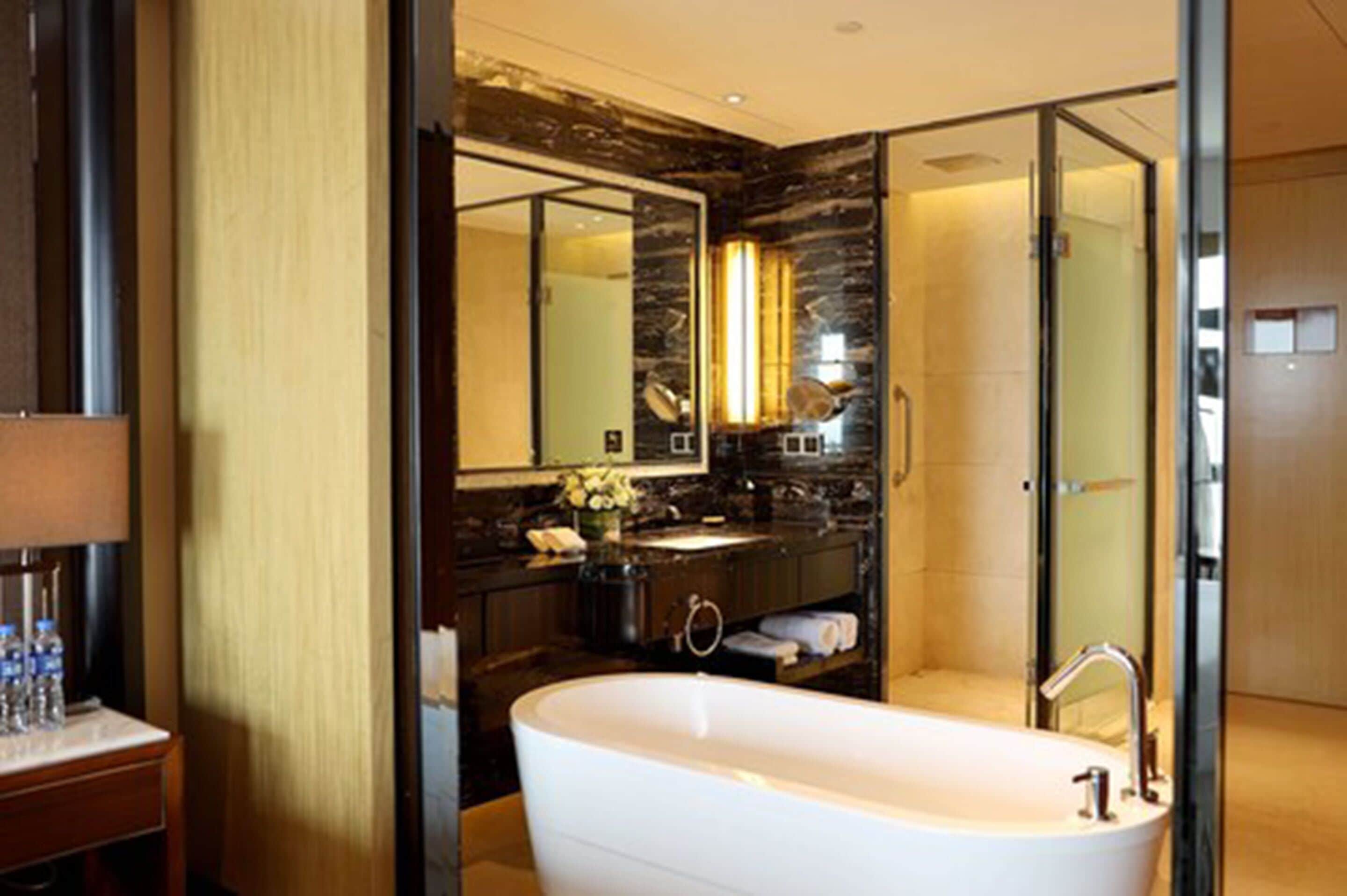 A modern bathroom with a freestanding bathtub, a large mirror, and a dark wood vanity.