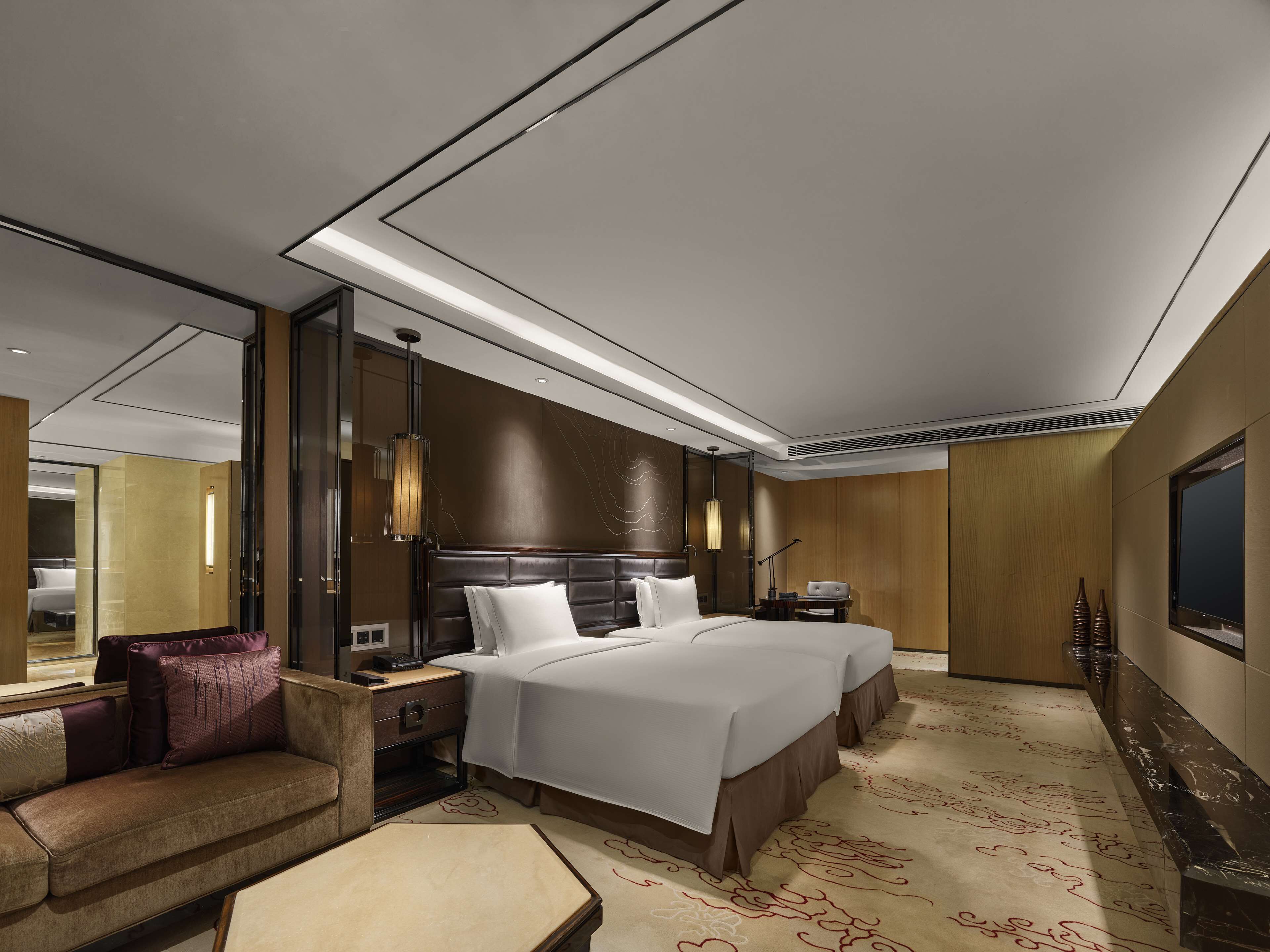 A modern hotel room with a large bed, a sofa, a desk, and a TV.