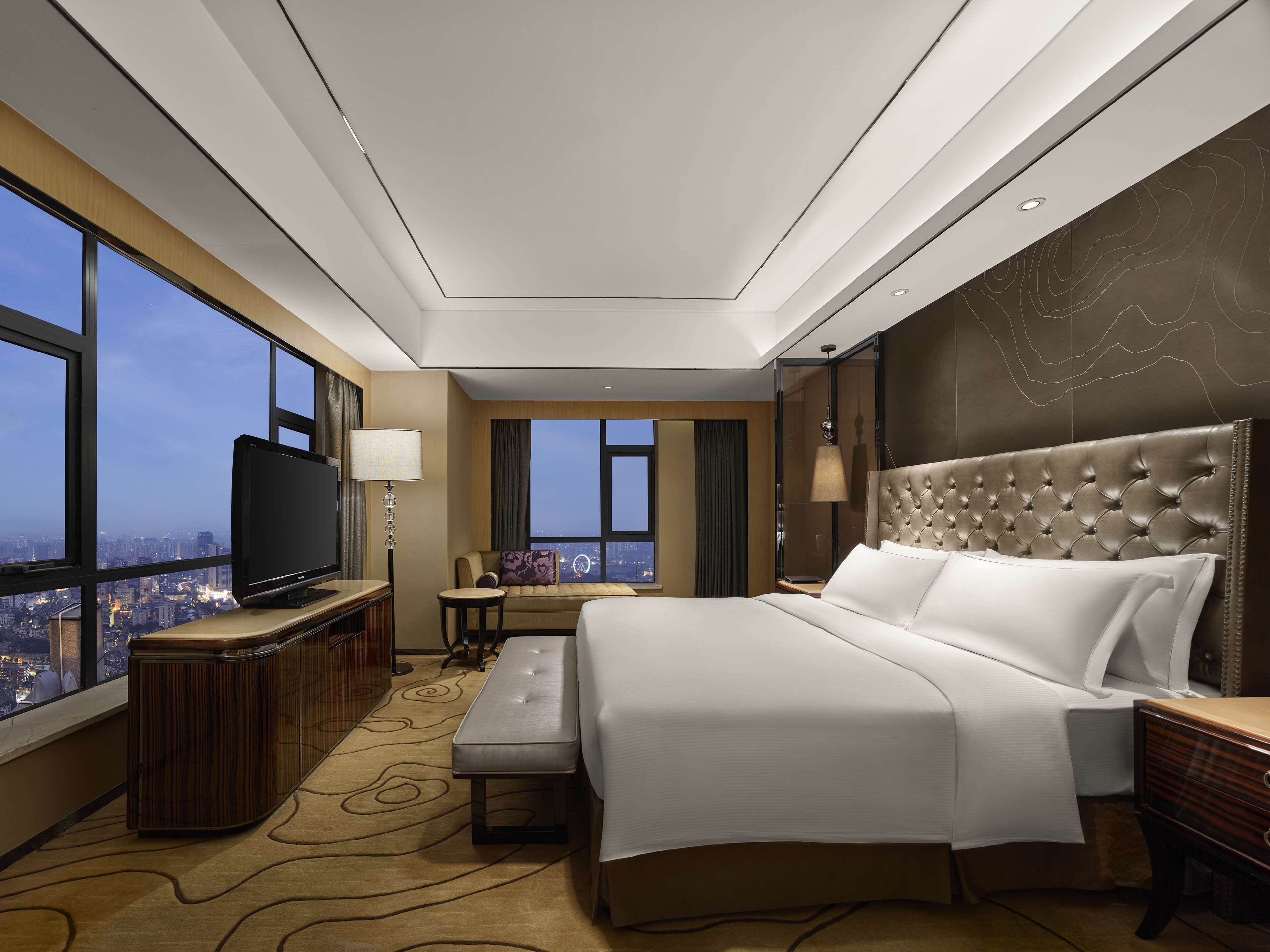 Una habitación de hotel moderna con una cama grande, televisión, sofá y vistas a la ciudad.