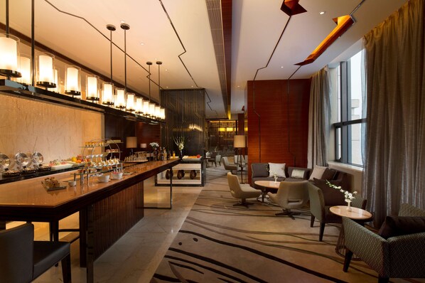 Un hall d’hôtel moderne doté d’un bar, de coins salon et d’une grande fenêtre.