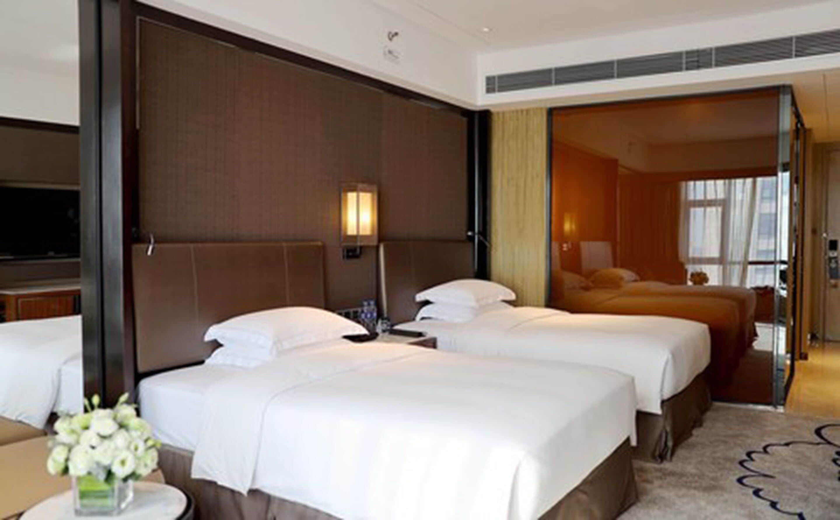 A hotel room with three beds, a TV, and a bathroom visible through an open door.