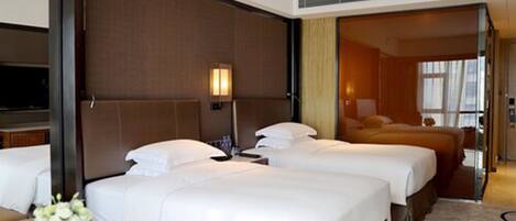A hotel room with three beds, a TV, and a bathroom visible through an open door.