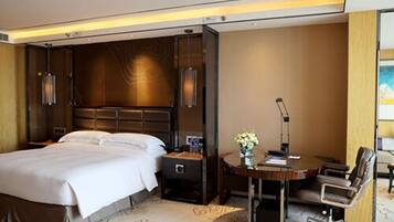 A hotel room with a large bed, a desk with a chair, a lamp, and a vase with flowers.
