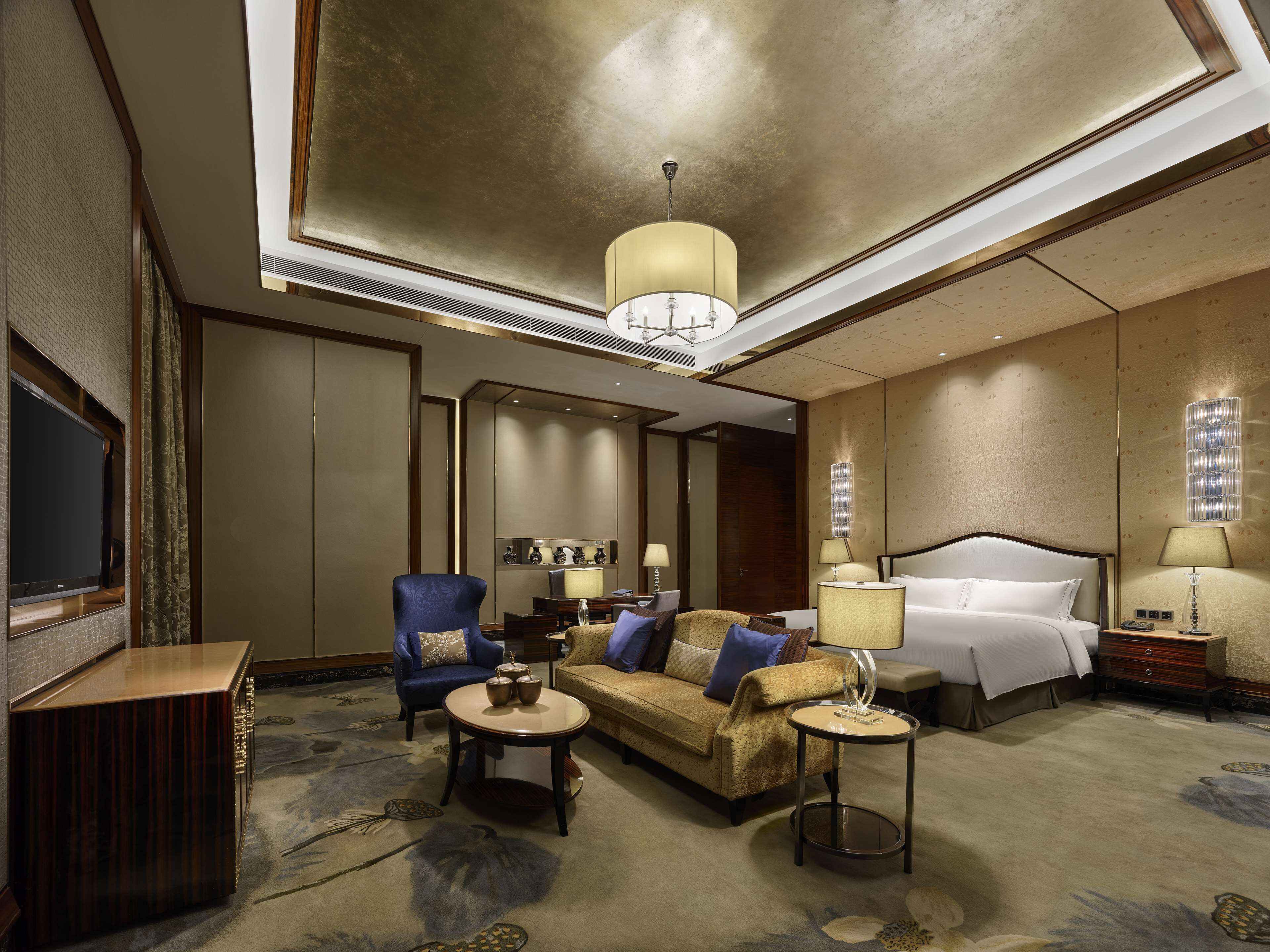A hotel room with a large bed, two sofas, a TV, and a chandelier.