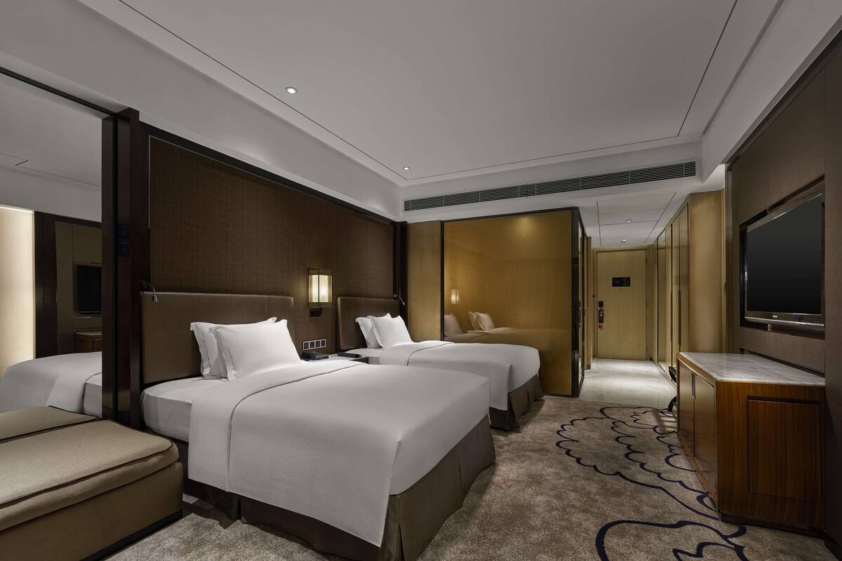Habitación de hotel con una cama grande, una cama más pequeña, un sofá, un televisor y un escritorio.